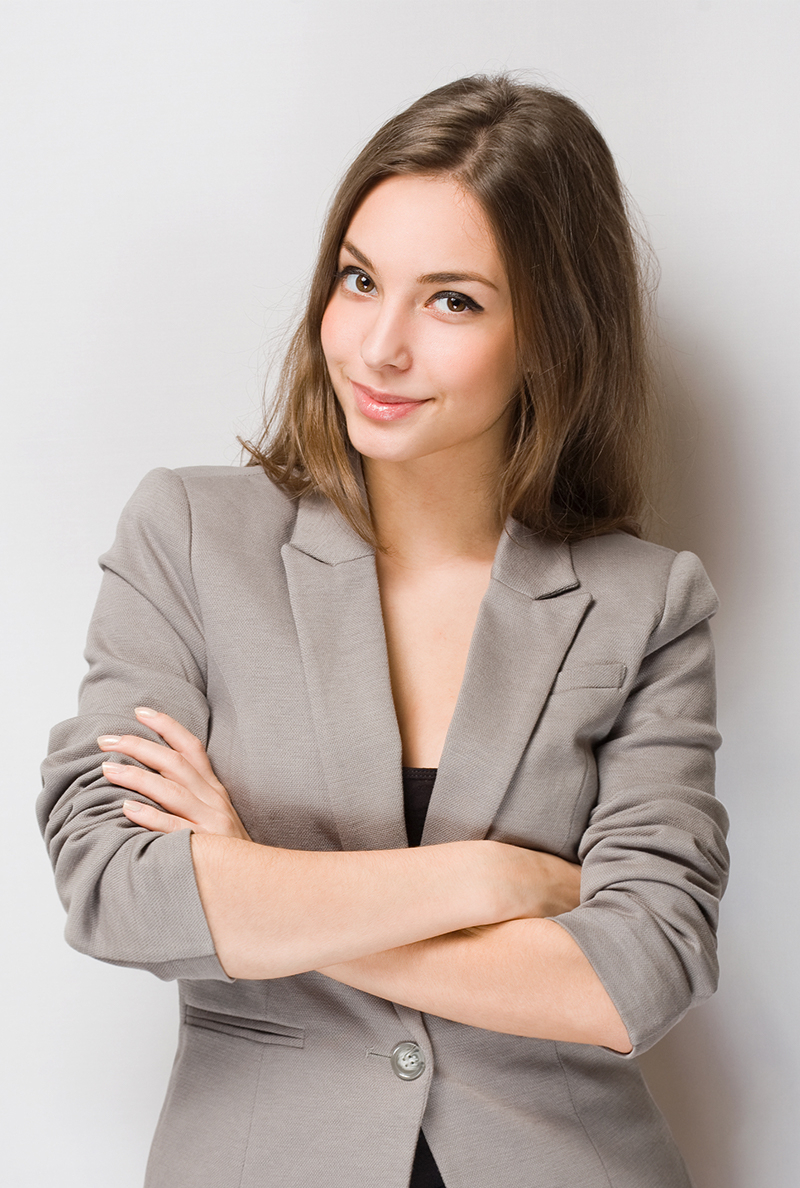 Young woman with long hair wearing a gray blazer and crossing her arms, smiling slightly.