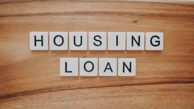 White letter tiles arranged to spell 'Housing Loan' on a wooden surface.