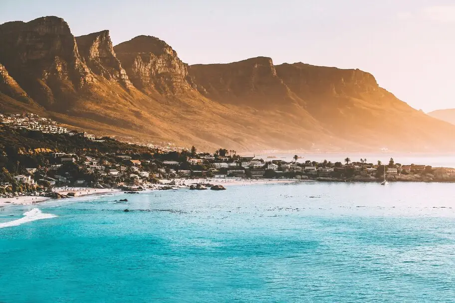 Scenic coastal view of Cape Town featuring mountains and ocean under a sunset sky.