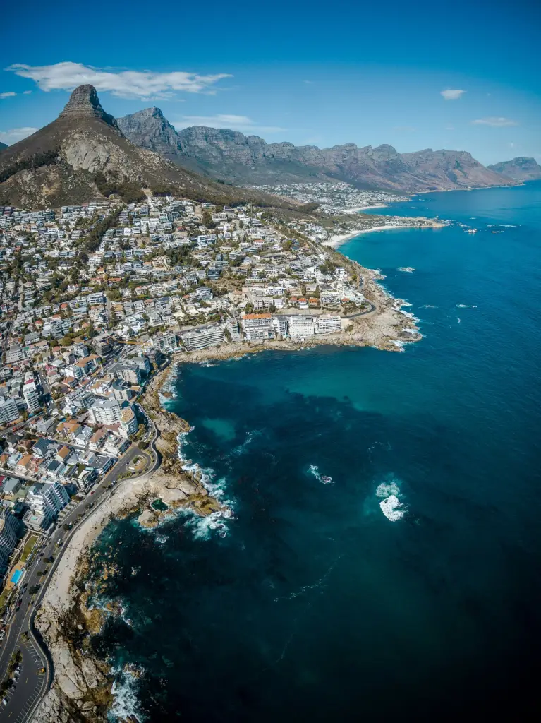Aerial view of the coastline of Cape Town with mountains in the background and clear blue water.