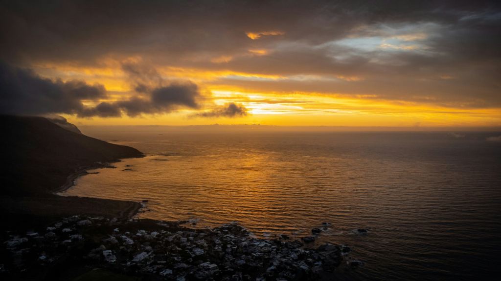 A scenic view of a sunset over the ocean with clouds and a coastal landscape.