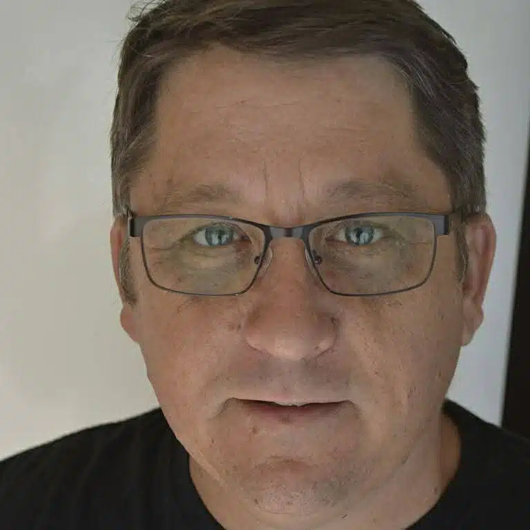 Close-up portrait of a man wearing glasses and a black shirt with short hair.